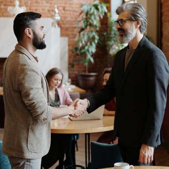 Two men in buisness attire in a coffee shop shaking hands