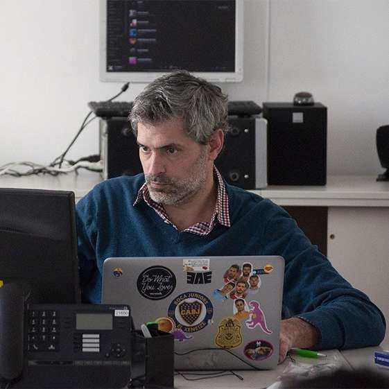 Man in a buisness environment working on a laptop and a desktop computer. There's a desk phone in the forground.